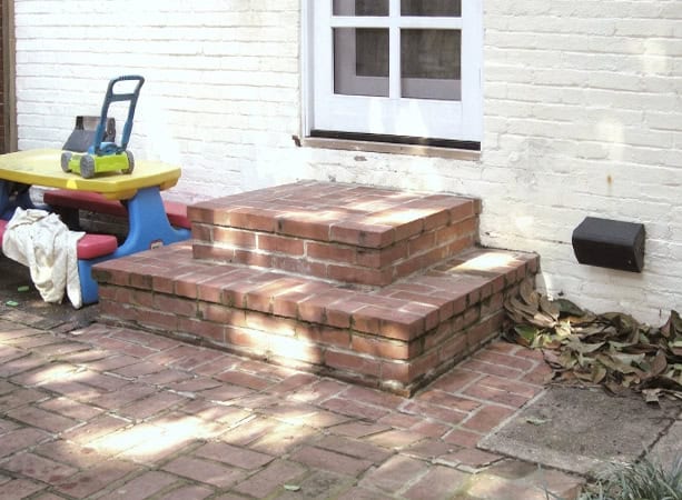 Brick masonry steps leading to a white house door with a window, showcasing historic tuckpointing an.