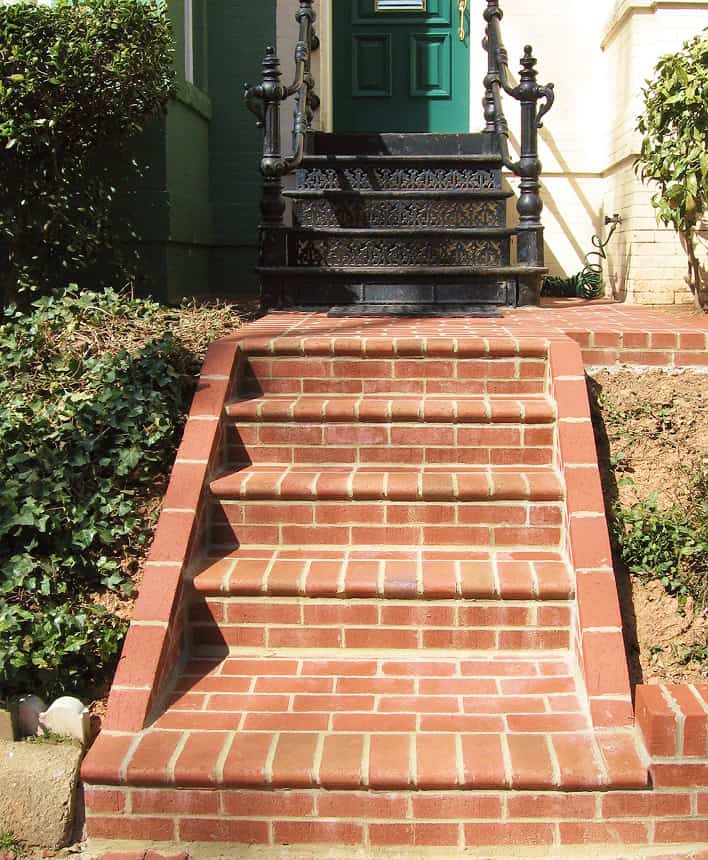 Historic brick stairs with black wrought iron railing at a residential entrance.