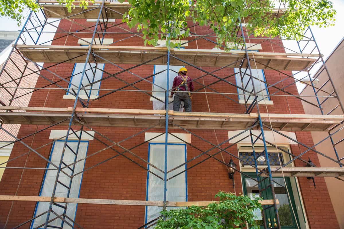 Worker on scaffolding repairing brick masonry on historic building facade.