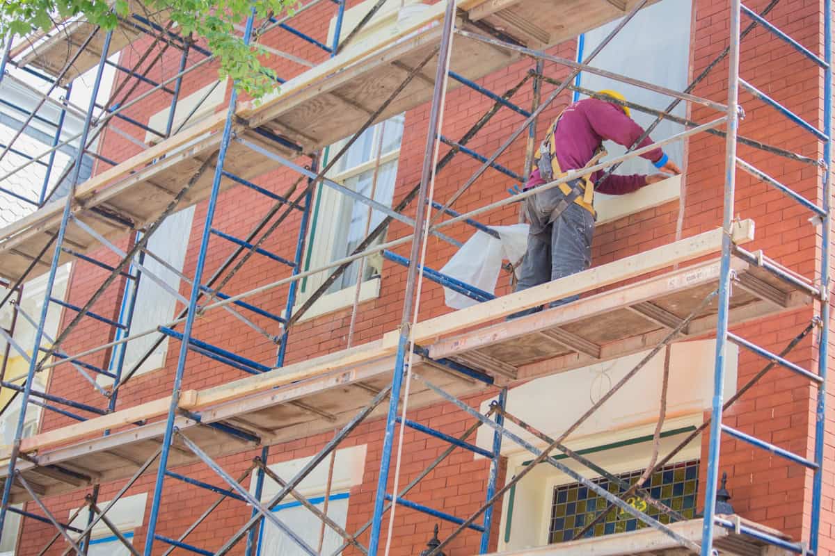 Mason performing tuckpointing on historic brick building facade.