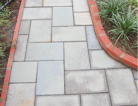 Close-up of a newly installed stone walkway with brick edging and garden plants.