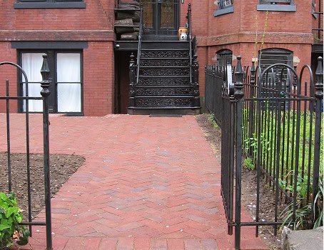 Historic brick pathway with black wrought iron fence and stairs.