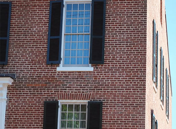 Close-up of a historic brick building with black shutters and large windows.