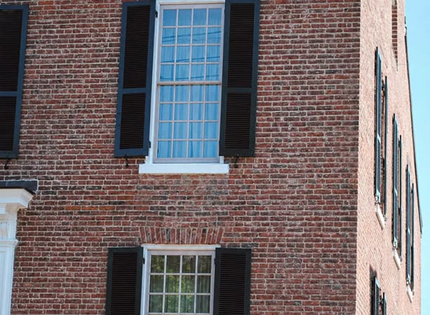 Close-up of historic brick masonry with black shutters and large window.